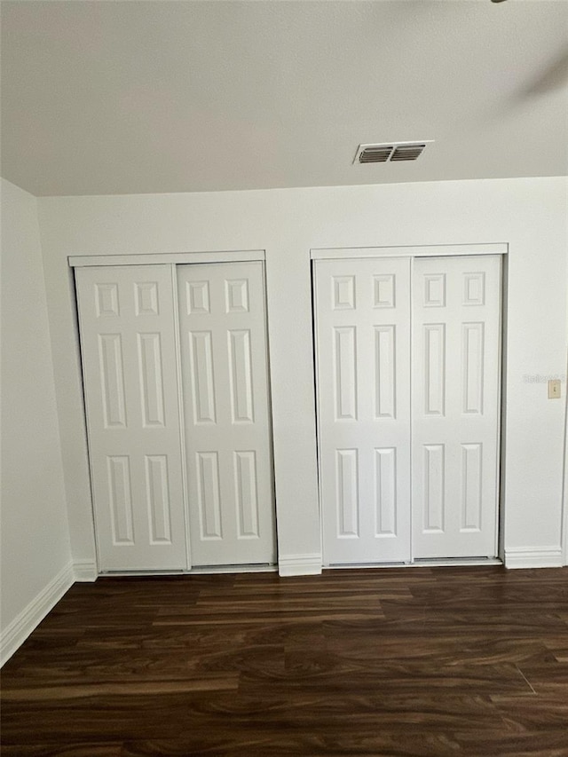 unfurnished bedroom featuring baseboards, visible vents, dark wood-style flooring, and two closets