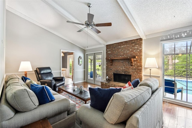 living room with vaulted ceiling with beams, a brick fireplace, ceiling fan, a textured ceiling, and wood finished floors