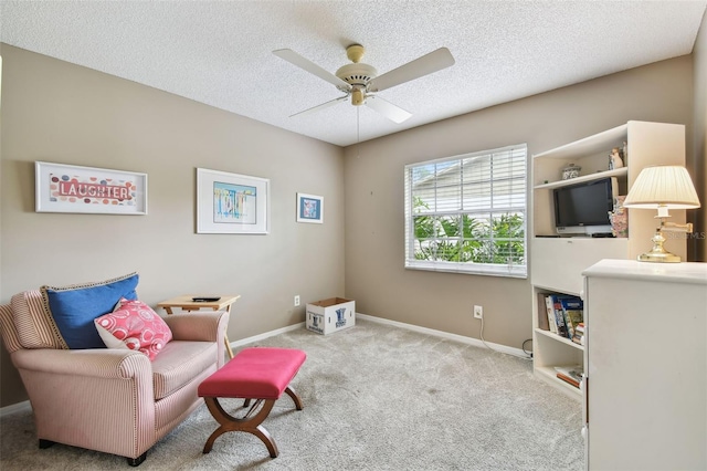 living area with a ceiling fan, light carpet, a textured ceiling, and baseboards