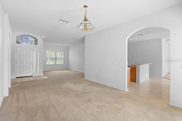 interior space with light tile patterned floors, visible vents, arched walkways, light colored carpet, and a textured ceiling