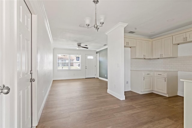 kitchen featuring ceiling fan with notable chandelier, wood finished floors, light countertops, ornamental molding, and backsplash