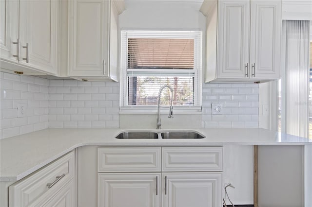 kitchen featuring light stone counters, white cabinetry, a sink, and backsplash