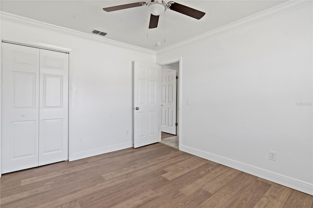 unfurnished bedroom featuring baseboards, a textured ceiling, crown molding, light wood-type flooring, and a closet