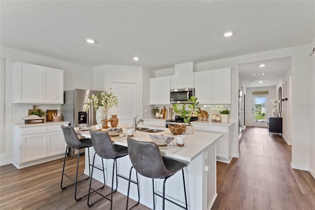 kitchen with stainless steel appliances, a sink, white cabinets, light countertops, and a center island with sink