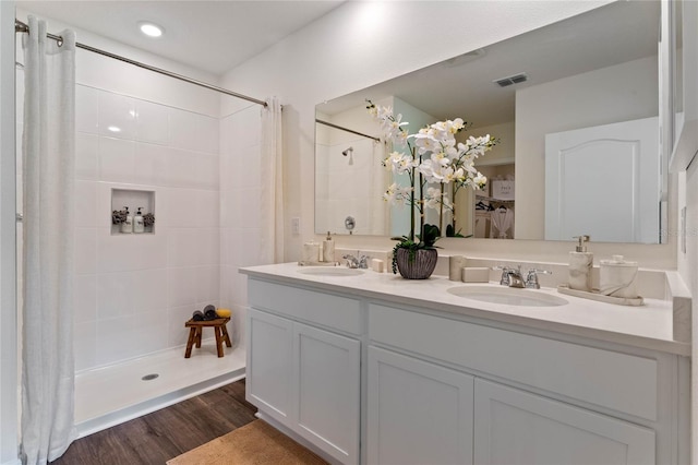 bathroom with wood finished floors, tiled shower, a sink, and visible vents