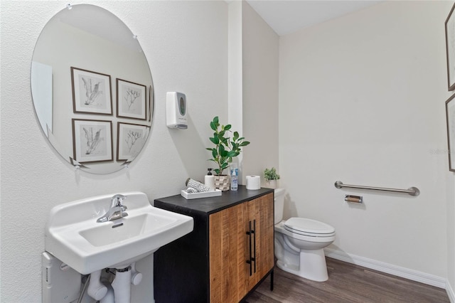 half bath with toilet, a sink, baseboards, and wood finished floors