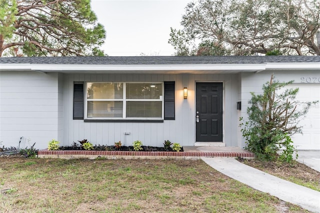 entrance to property with a garage, roof with shingles, and a lawn