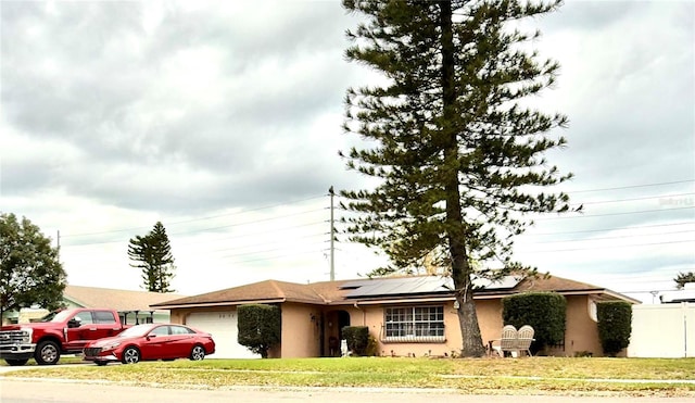 single story home featuring solar panels, a front lawn, an attached garage, and stucco siding