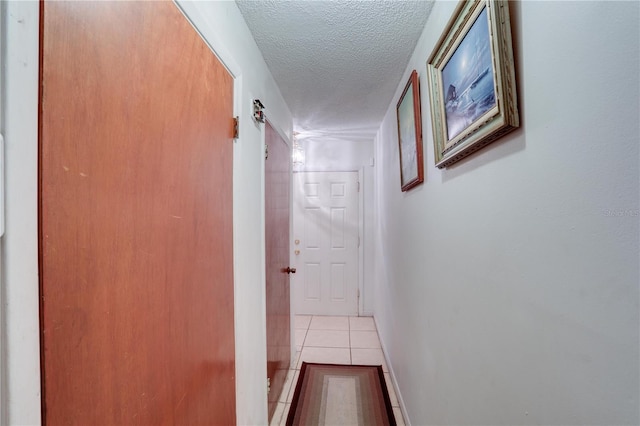 hall with a textured ceiling, baseboards, and tile patterned floors