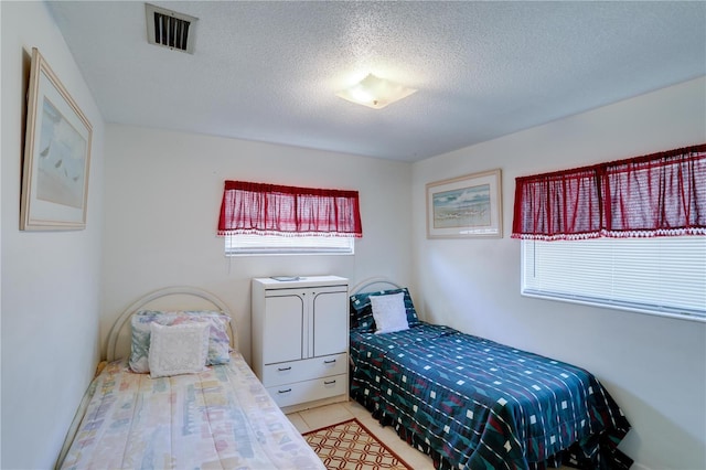 bedroom with visible vents, a textured ceiling, and light tile patterned flooring