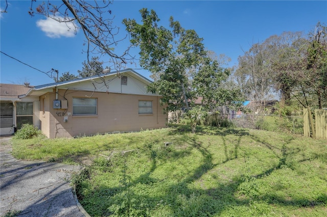 view of side of property with a lawn, concrete block siding, and fence