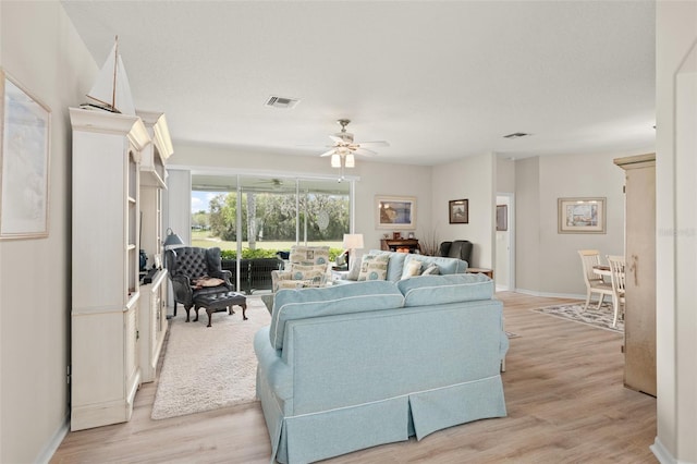 living room with a ceiling fan, visible vents, light wood finished floors, and baseboards