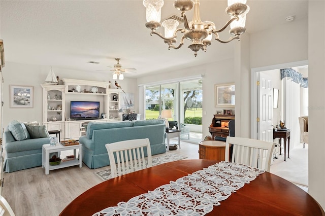 dining space featuring ceiling fan with notable chandelier and light wood-style floors