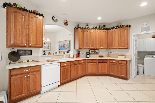 kitchen with washer / dryer, brown cabinetry, visible vents, and white dishwasher