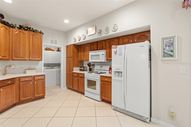 kitchen featuring visible vents, white appliances, brown cabinetry, and washer and clothes dryer