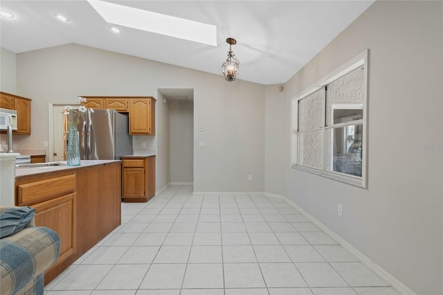 kitchen featuring vaulted ceiling with skylight, white microwave, freestanding refrigerator, light countertops, and light tile patterned flooring