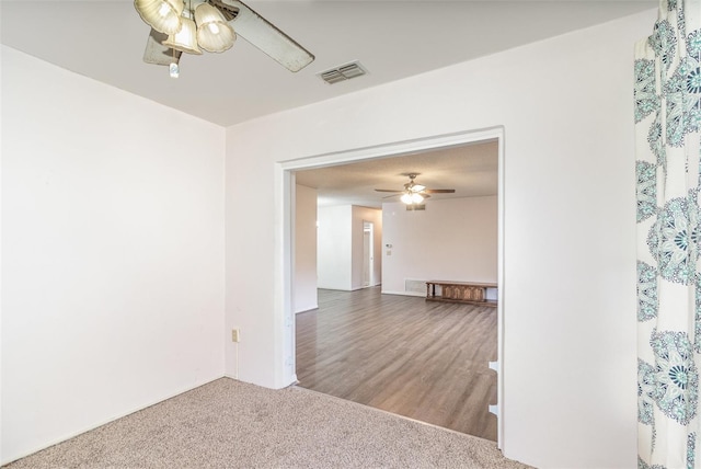 unfurnished room featuring visible vents, wood finished floors, a ceiling fan, and carpet flooring