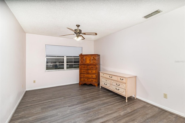 unfurnished bedroom with a textured ceiling, dark wood-type flooring, visible vents, and baseboards