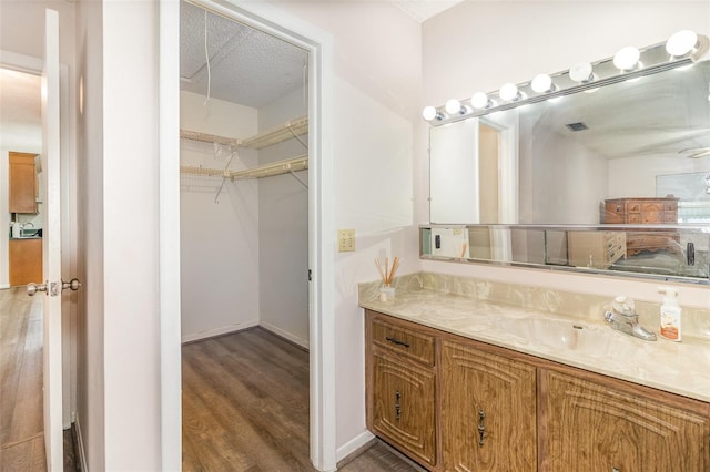 bathroom featuring visible vents, baseboards, wood finished floors, a spacious closet, and vanity