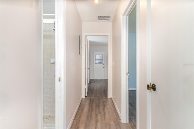 hall with baseboards, visible vents, and wood finished floors