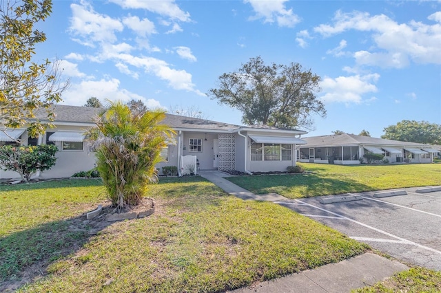 ranch-style home featuring uncovered parking, a front lawn, a sunroom, and stucco siding