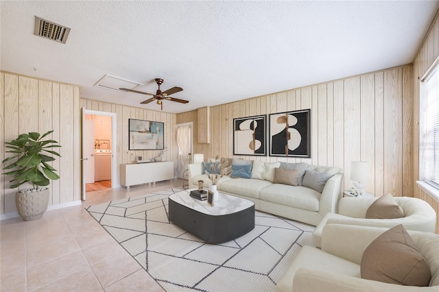 living room featuring light tile patterned floors, wooden walls, visible vents, a ceiling fan, and a textured ceiling