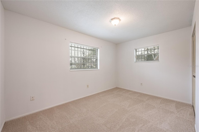 empty room with light carpet, a textured ceiling, and baseboards