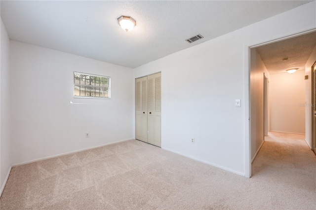 unfurnished bedroom featuring a closet, visible vents, light carpet, a textured ceiling, and baseboards