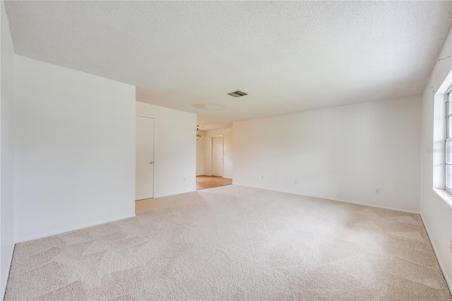 unfurnished room with light carpet, visible vents, and a textured ceiling