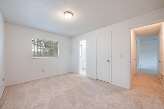 unfurnished bedroom featuring light carpet, a textured ceiling, ensuite bath, and baseboards