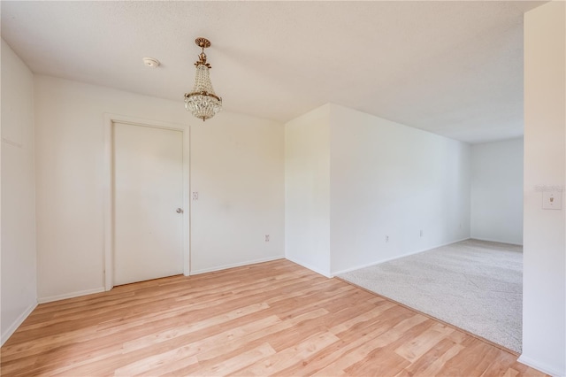 unfurnished room with a chandelier, baseboards, and light wood finished floors