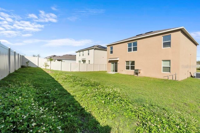 back of property with central air condition unit, a fenced backyard, a lawn, and stucco siding