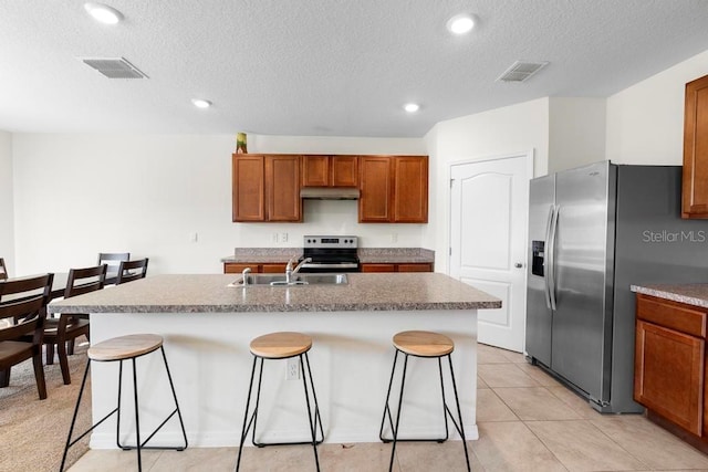 kitchen with stainless steel appliances, a breakfast bar, an island with sink, and under cabinet range hood