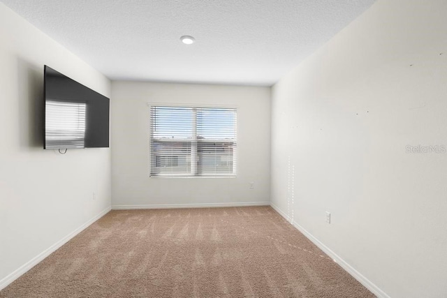 spare room featuring light carpet, a textured ceiling, and baseboards