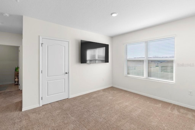 carpeted spare room featuring a textured ceiling and baseboards