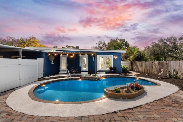 pool at dusk with a fenced in pool, a patio area, french doors, and a fenced backyard