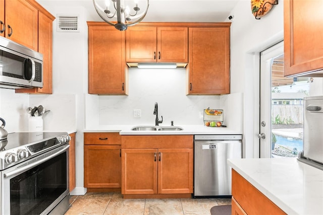 kitchen with stainless steel appliances, light countertops, visible vents, brown cabinetry, and a sink