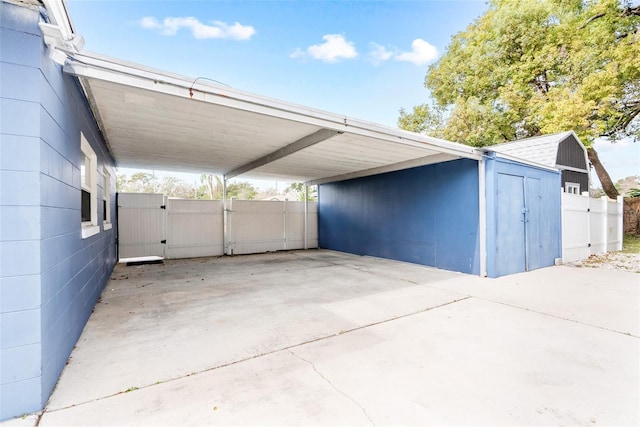 garage with an attached carport, fence, concrete driveway, a gate, and a shed