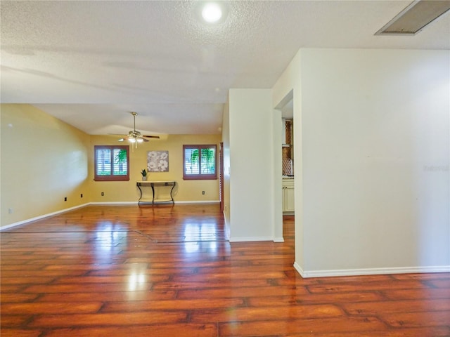 empty room featuring visible vents, baseboards, a ceiling fan, dark wood-type flooring, and a textured ceiling