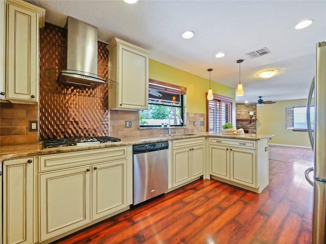 kitchen featuring stainless steel appliances, a peninsula, a sink, cream cabinetry, and wall chimney exhaust hood