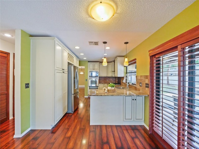 kitchen featuring light stone counters, a peninsula, dark wood-style flooring, hanging light fixtures, and appliances with stainless steel finishes