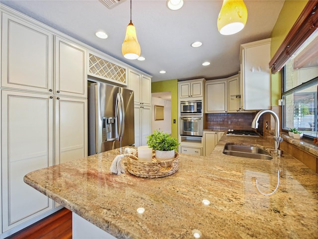 kitchen with light stone counters, a sink, appliances with stainless steel finishes, tasteful backsplash, and decorative light fixtures