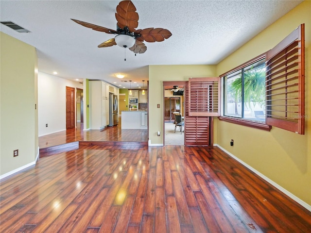 unfurnished living room featuring ceiling fan, visible vents, dark wood finished floors, and a textured ceiling