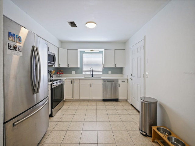 kitchen with light tile patterned floors, appliances with stainless steel finishes, light countertops, white cabinetry, and a sink