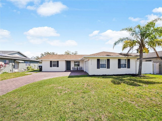 ranch-style house with decorative driveway, fence, and a front lawn