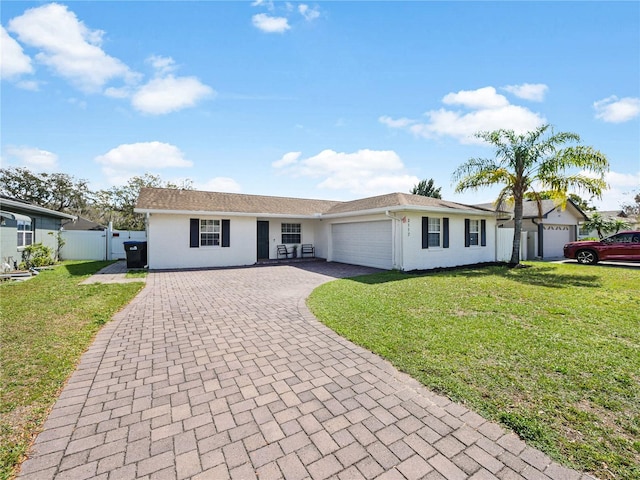 ranch-style house with an attached garage, fence, a front lawn, and decorative driveway