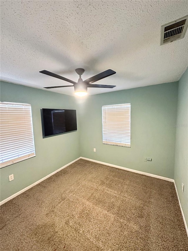 carpeted empty room featuring baseboards, a textured ceiling, visible vents, and a ceiling fan