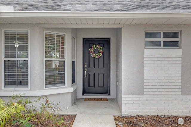 property entrance featuring a shingled roof and stucco siding