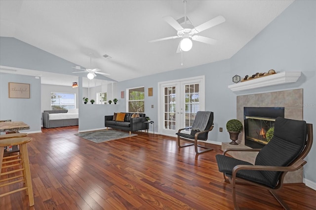 sitting room with a tiled fireplace, a ceiling fan, lofted ceiling, dark wood-type flooring, and french doors