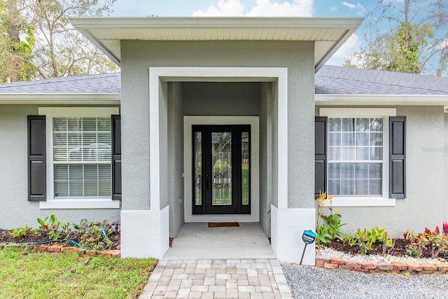 view of exterior entry with roof with shingles and stucco siding